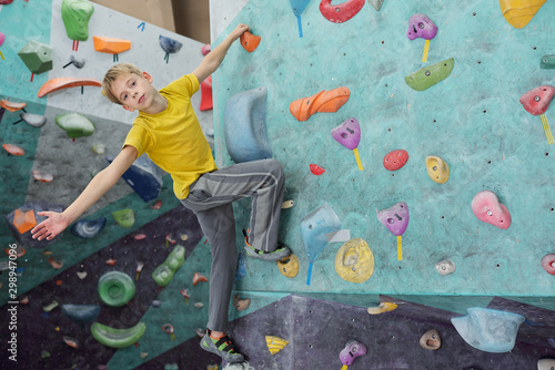 Cute youngster looking at you while holding by small rock on climbing wall
