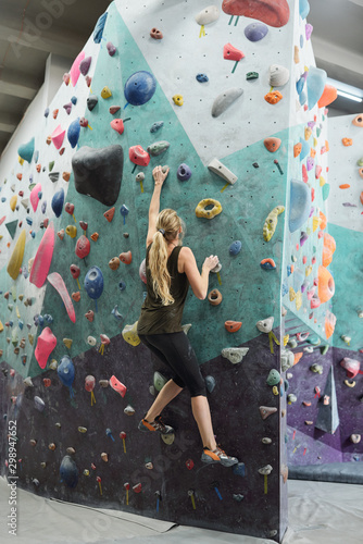 Young active woman with long hair grabbing by artificial rocks on climbing wall