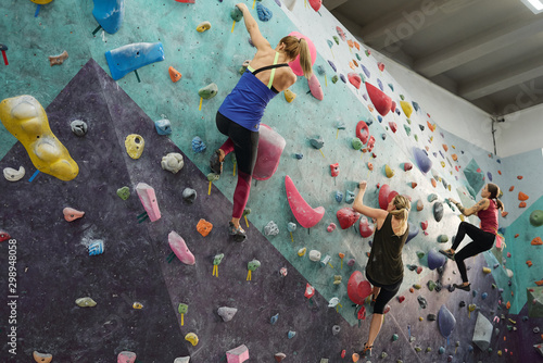 Three young sporty women in activewear grabbing by rocks on climbing equipment