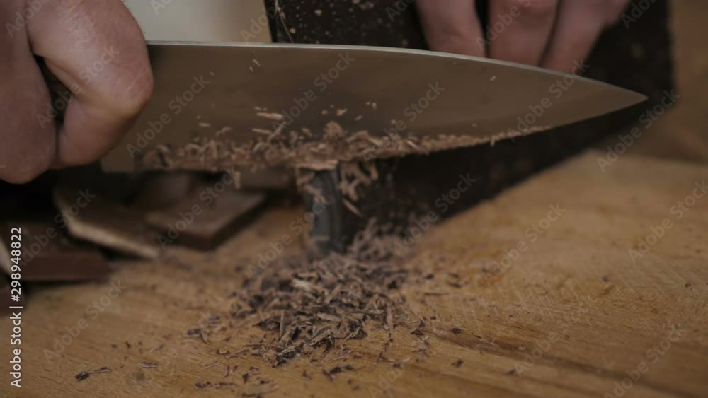 Chopped dark chocolate on kitchen board. Chopping a Bar of Chocolate while Making Baking. Slow motion. Close up. Chop chocolate on cutting board on wooden table . Closeup.
