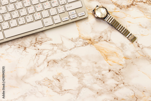 Modern aluminum computer keyboard and hand watch isolated on marble background