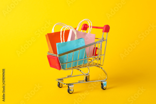 Small shopping cart with paper bags on yellow background, space for text