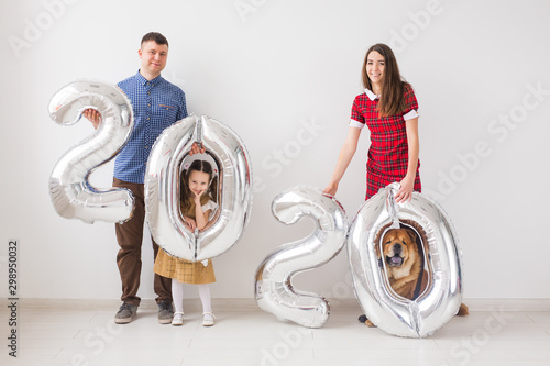 New 2020 Year is coming concept - Happy family with dog are holding silver colored numbers indoors.