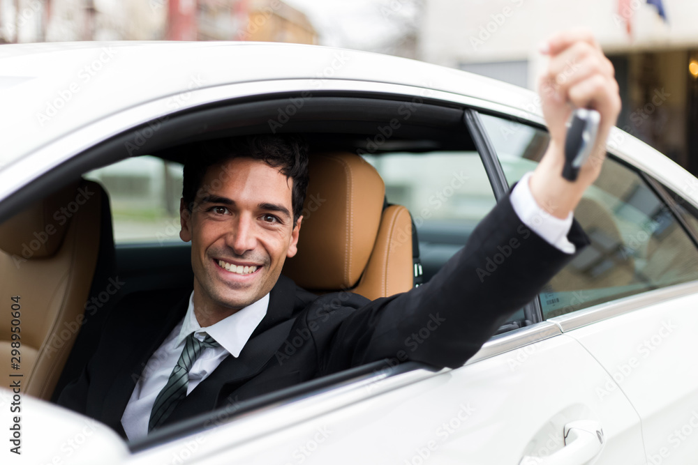 Young businessman smiling in his new car showing car keys
