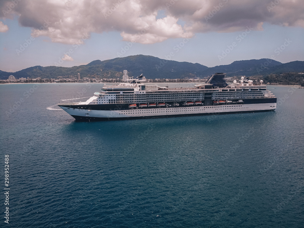 Beautiful cruise liner in the blue sea, treed slopes and coastal town on the background; luxury recreation concept. Beautiful cruise liner in the blue sea, treed slopes and coastal town on the background; luxury recreation concept.