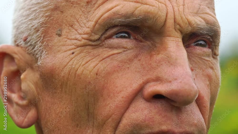 senior handsome gentle man brown eyes squint look up and blink extreme close view against blurry nature slow motion senior handsome gentle man brown eyes squint look up and blink extreme close view against blurry nature slow motion
