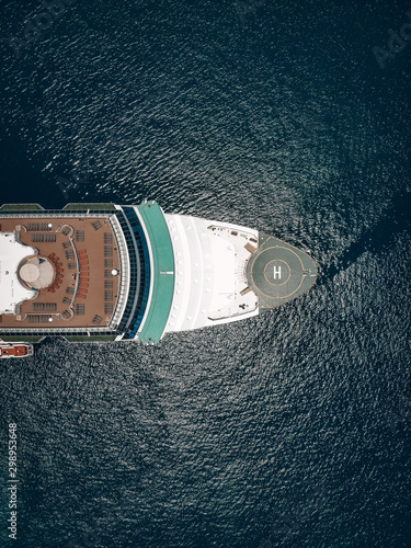 Drone view of the of the cruise liner, red-brick deck, helideck and deck-chairs, blue sunny sea with flecks around. Vessel equipment concept.