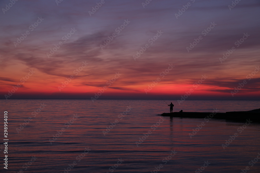 silhouette of a fisherman at sunset or sunrise. Bright colors of the sunset. Red sunset.