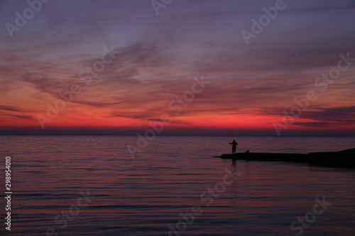 silhouette of a fisherman at sunset or sunrise. Bright colors of the sunset. Red sunset.