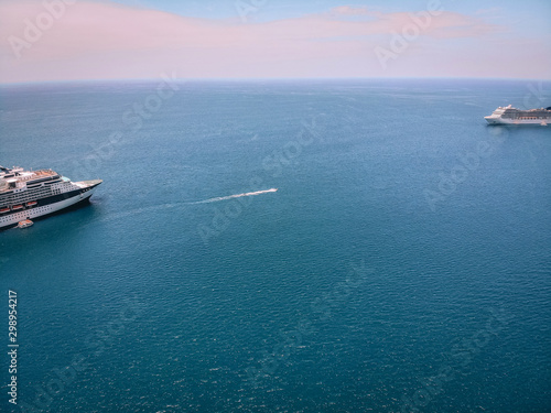 Drone shot of the snout of the cruise ships in a voyage by sea, boats nearby; horizon, vast blue waters.