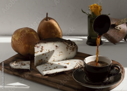 Cup with dark espresso on a gray background. Espresso is poured from a cezva into a cup. Near homemade (craft) goat cheese with walnuts and ripe pears. Close-up, dessert concept. photo