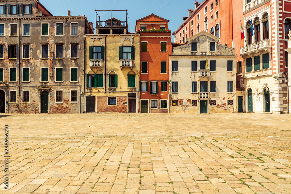 view at a square in Venice , covered with paving stones and old buildings with flags on thr background , tourism landscape