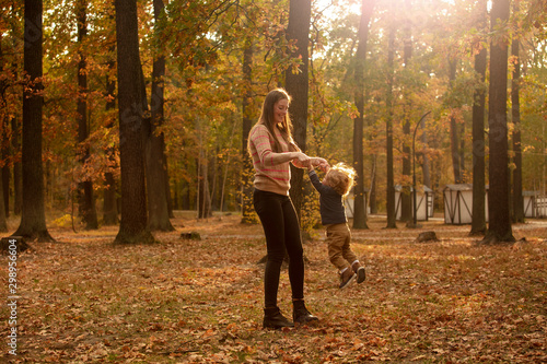 Happy mom is circling with her beautiful baby in the autumn park. Lifestyle. Happy emotions. Play in the park.