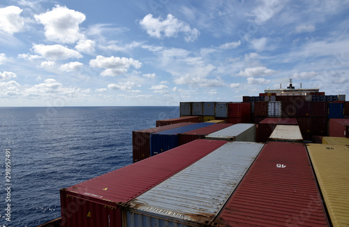Large, fully loaded, cargo container ship sailing through the ocean. View from the forward mast on the cargo deck and navigational bridge. 