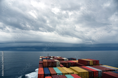 Container ship loaded with containers sailing through Pacific Ocean towards a stormy clouds. 