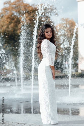 Fashion gorgeous woman in beautiful dress. Luxury girl with dark long hair and nude makeup, elegant fashionable lady, vogue style female. Sexy girl near the fountain.