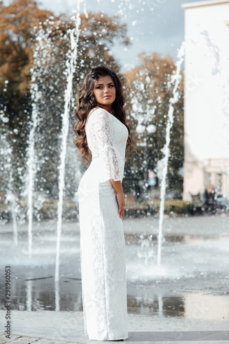 Fashion gorgeous woman in beautiful dress. Luxury girl with dark long hair and nude makeup, elegant fashionable lady, vogue style female. Sexy girl near the fountain.