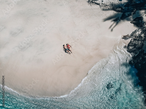 Aerial view of the loving couple lying on the sandy beach, turquoise water; honeymoon concept.