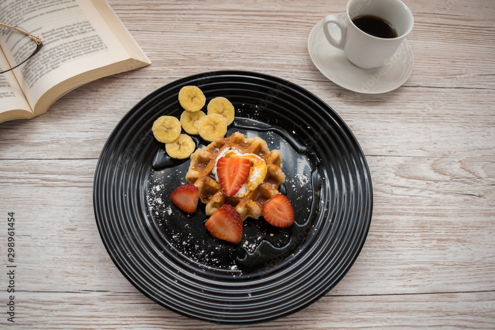 Belgian waffle with fruit and cream on a table with a book and a cup of coffee Belgian waffle with fruit and cream on a table with a book and a cup of coffee