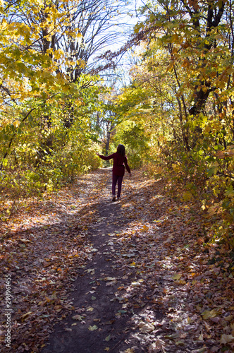 Girl walking on autumn forest pathway among yellow and orange trees, beauty of nature. © Olga Biliak