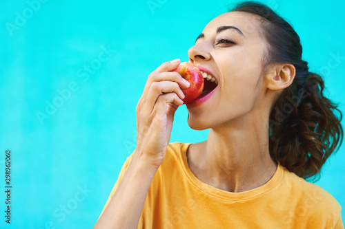 Portrait of healthy young woman biting juicy ripe apple with delighte  healthy snack fresh ripe  posing on a colorful bright cyan background.