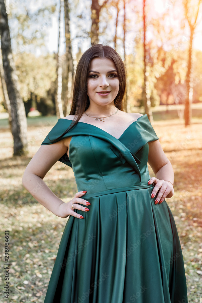 Young woman wearing fashionable green dress walking in autumn park.