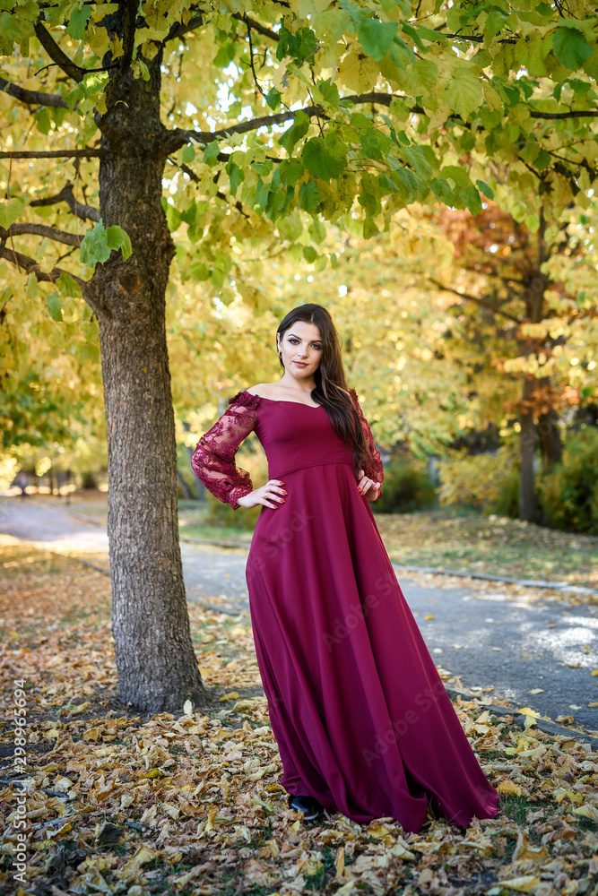 Young princess in a beautiful red dress in park. The background is bright, golden autumn nature. Young princess in a beautiful red dress in park. The background is bright, golden autumn nature.