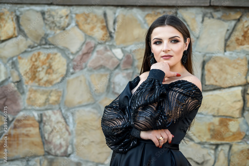 Fashion smiling woman in black dress on a brick background. Fashion