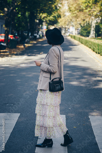 fashion blogger street style. fashionable woman posing wearing an oversized blazer, floral vintage dress, black ankle boots and a black trendy mini handbag. detail of a perfect fall 2019 outfit. 