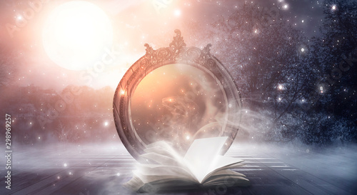 An open book and a magic mirror against the backdrop of a night landscape. Abstract dark scene, mystical background, fantasy. photo