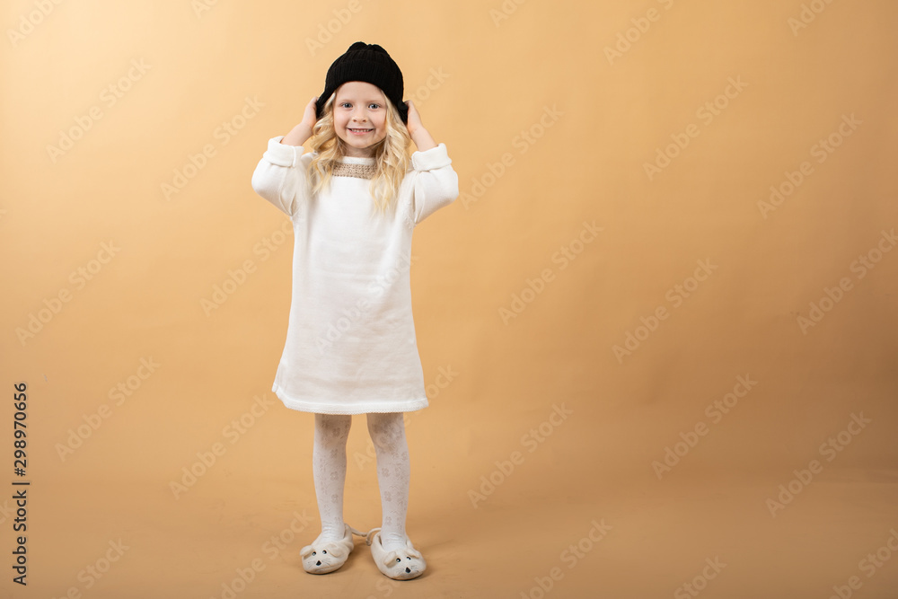 A little girl in a white knitted dress and a black hat. Very nice and cheerful girl A little girl in a white knitted dress and a black hat. Very nice and cheerful girl