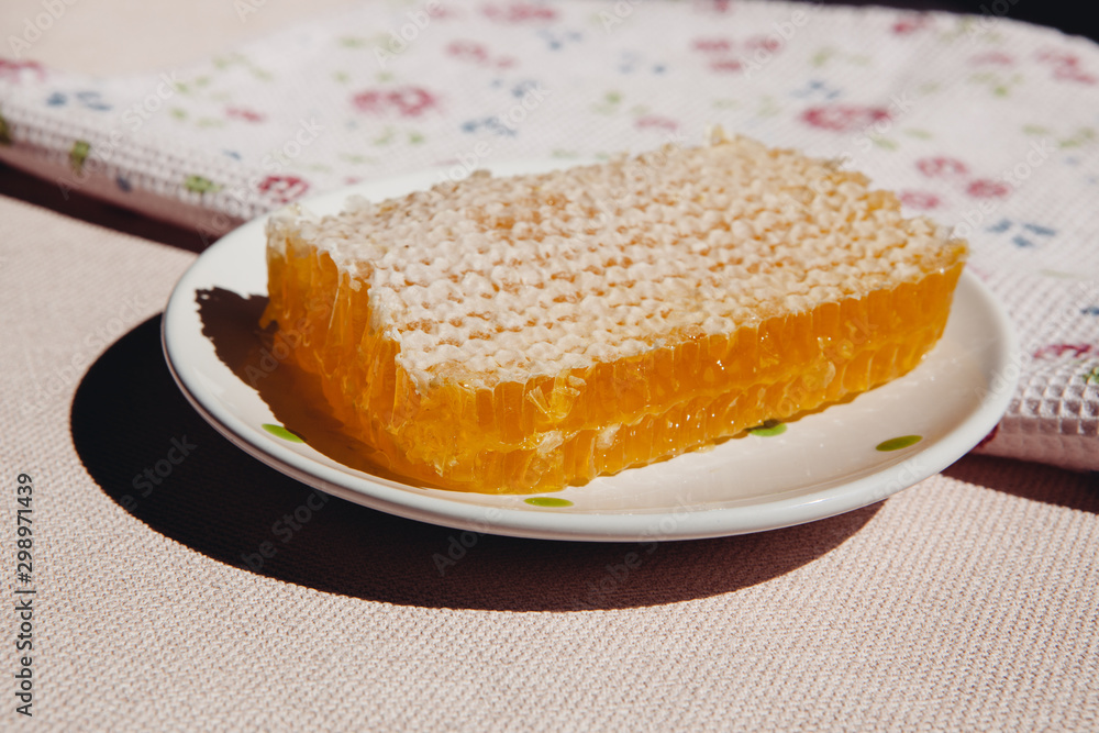Honey comb on plate on table with sunshine on background, healthy sweet food Honey comb on plate on table with sunshine on background, healthy sweet food