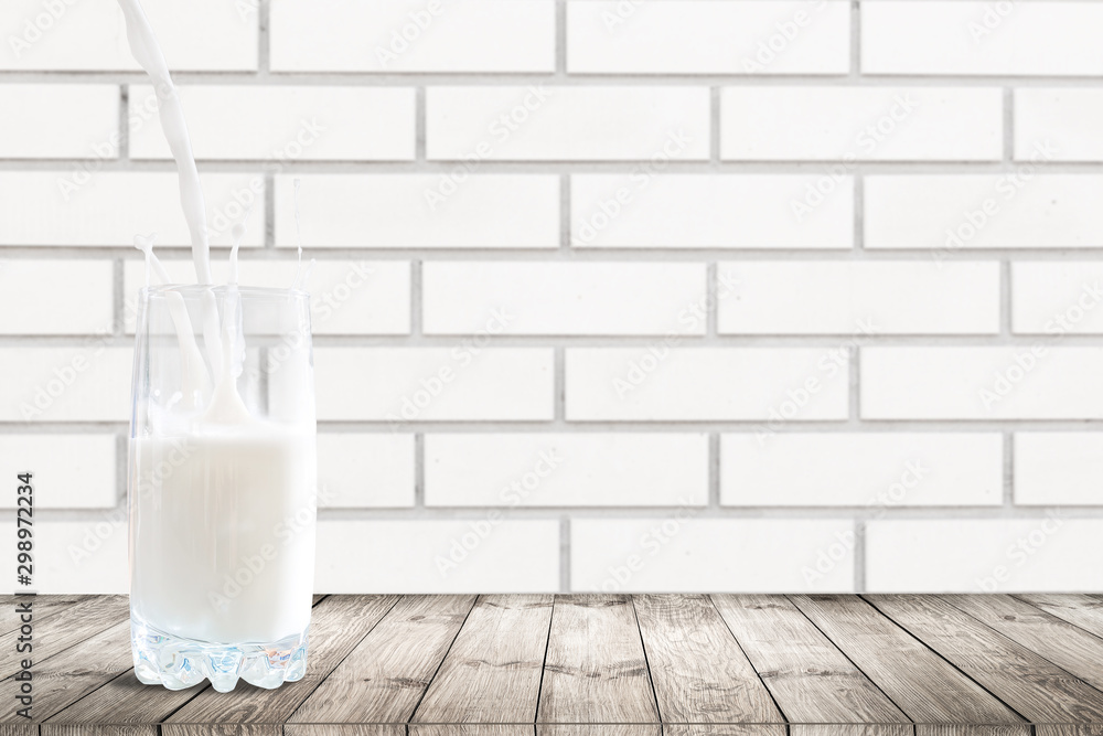 Splashes of milk in a glass on a white surface. Milk is poured into the glass infront of a white wooden background. Splashes of milk in a glass on a white surface. Milk is poured into the glass infront of a white wooden background.