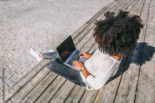 Brunette girl with afro hair and casual clothes works with her laptop in an outdoor area