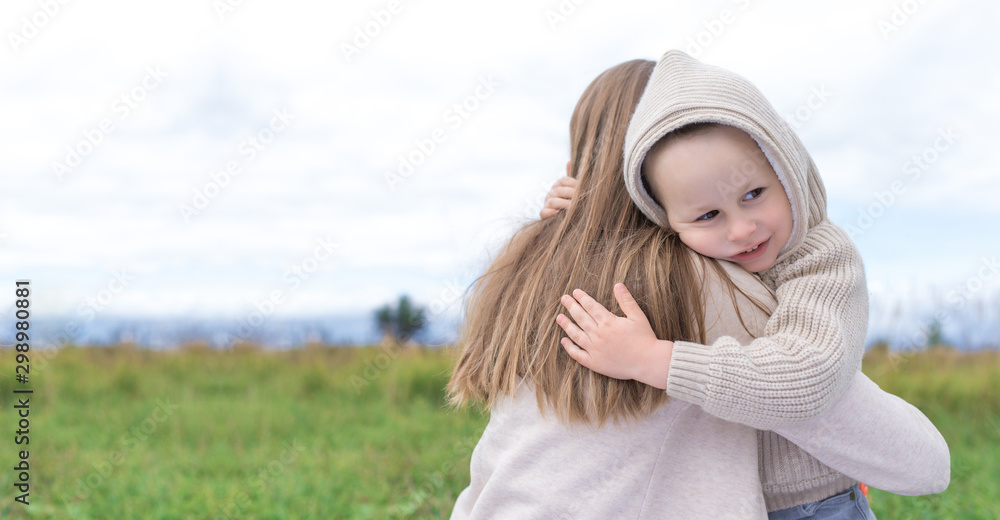 Happy family mom woman with little boy hugging at weekend. Hug, background green grass. Warm casual wear, hooded sweater. Caring support love and nurturing tenderness. Free space for text. Happy family mom woman with little boy hugging at weekend. Hug, background green grass. Warm casual wear, hooded sweater. Caring support love and nurturing tenderness. Free space for text.