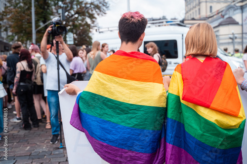 A couple with lgbt flags on their shoulders holding a poster