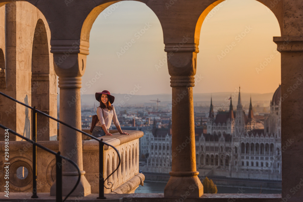 Naklejka premium Szczęśliwa młoda kobieta ciesząca się wycieczką do zamku w Budapeszcie na Węgrzech z punktu widokowego z Baszty Rybackiej o wschodzie słońca.