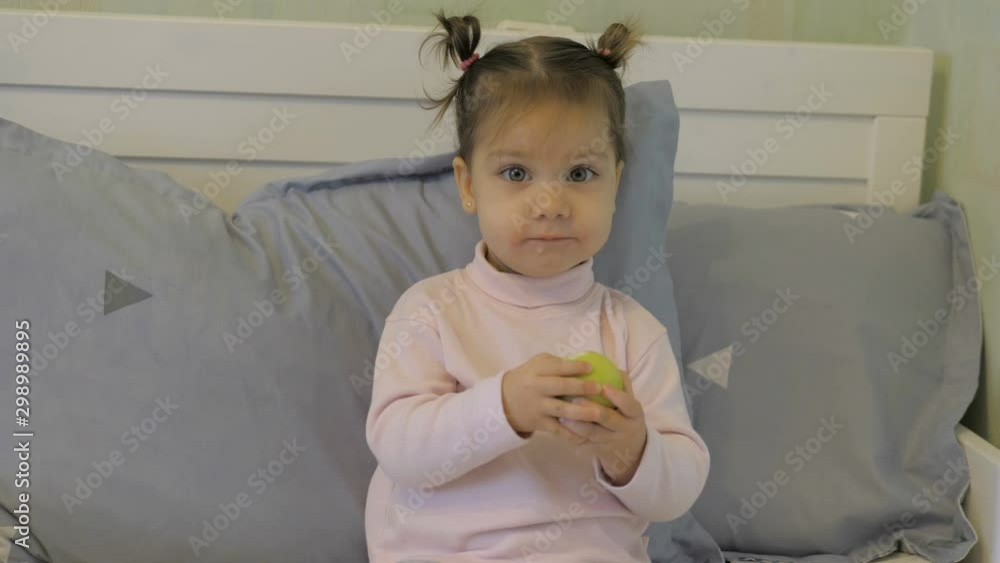 Cute little girl in bed eating apple and posing for the camera Cute little girl in bed eating apple and posing for the camera