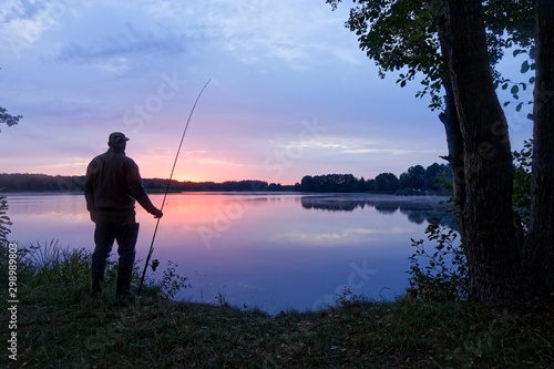 Fotografija Silhouette fisherman standing on the shore of the lake during dawn