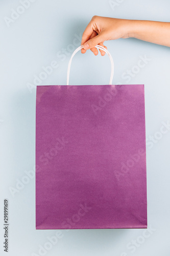 Female hand holding violet paper bag isolated on blue background