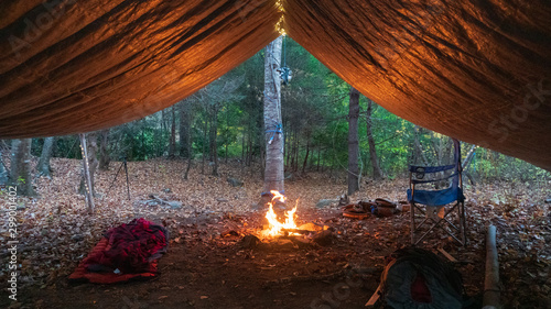 Fototapeta Naklejka Na Ścianę i Meble -  Primitive Tarp Shelter with campfire and fairy lights. Survival Bushcraft setup in the Blue Ridge Mountains near Asheville. During autumn / fall season.