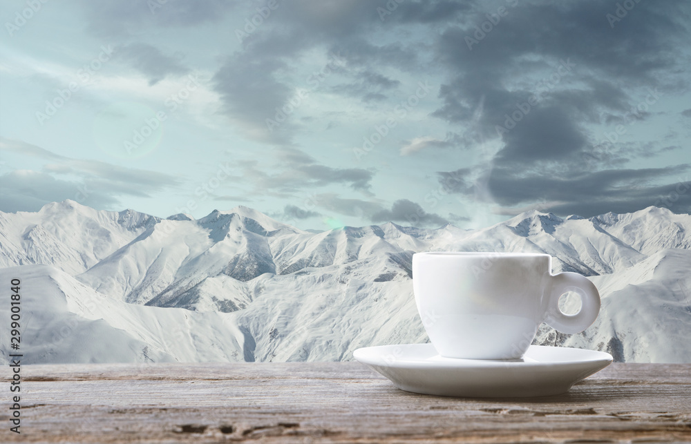 Single tea or coffee mug and landscape of mountains on background. Cup of hot drink with snowly look and cloudly sky in front of it. Warm in winter day, holidays, travel, New Year and Christmas time.