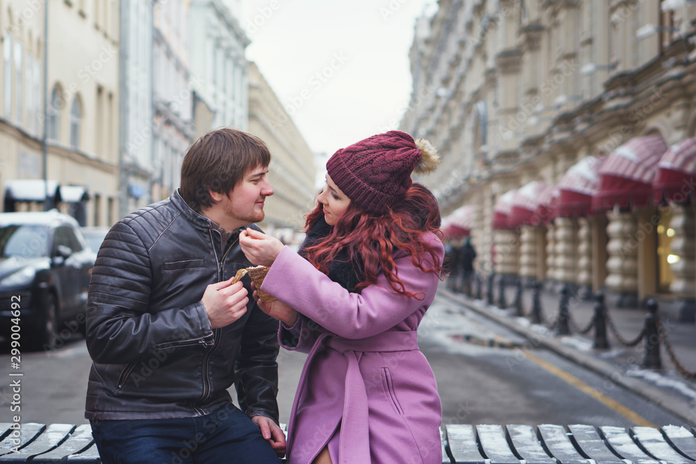 Obraz premium Portrait of beautiful young couple eating Trdelník in the street. Having fun in winter of the european city. Vacation and holiday concept