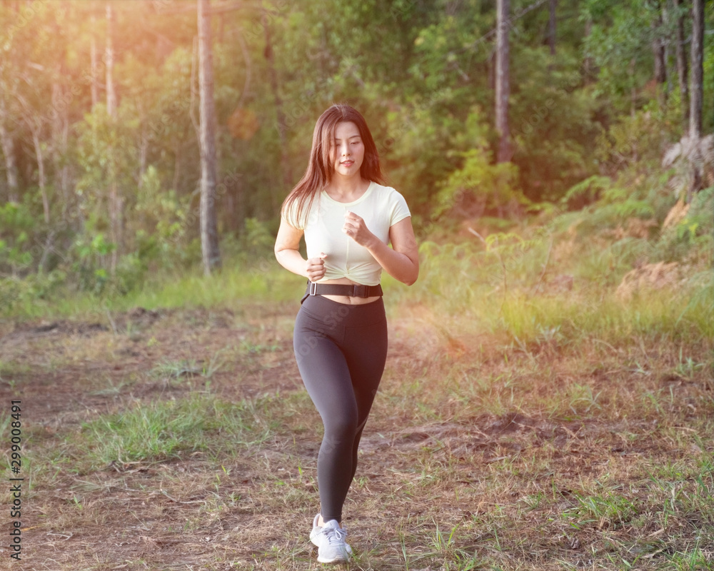 Young Asian woman wears sport black leggings runs on rural road in tropical  rain forest in