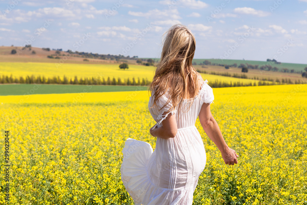 Φωτογραφία Woman in white dress looking out over fields of golden canola
