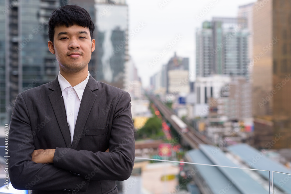 Portrait of young Asian businessman against view of the city Portrait of young Asian businessman against view of the city