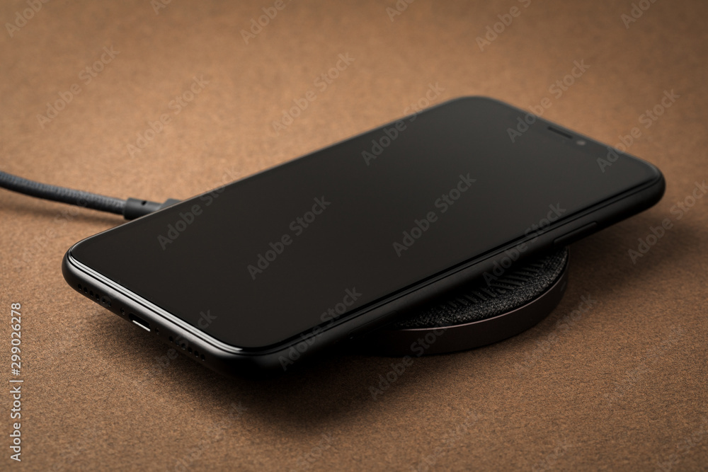 The smartphone is charged by a wireless charger on a brown background. Concept of new technologies. The smartphone is charged by a wireless charger on a brown background. Concept of new technologies.
