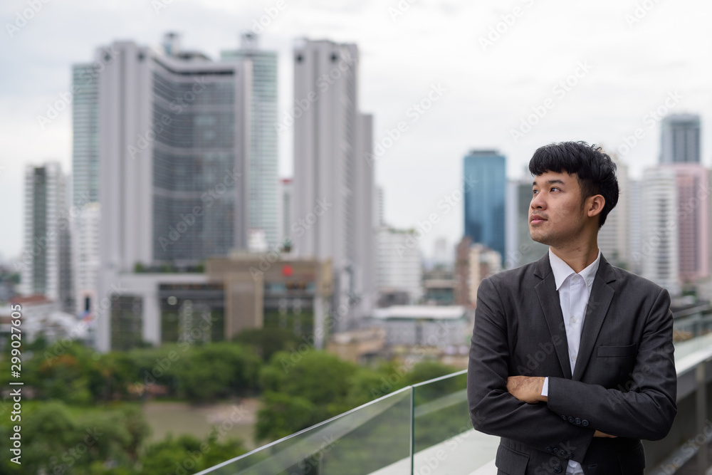 Portrait of young Asian businessman against view of the city Portrait of young Asian businessman against view of the city