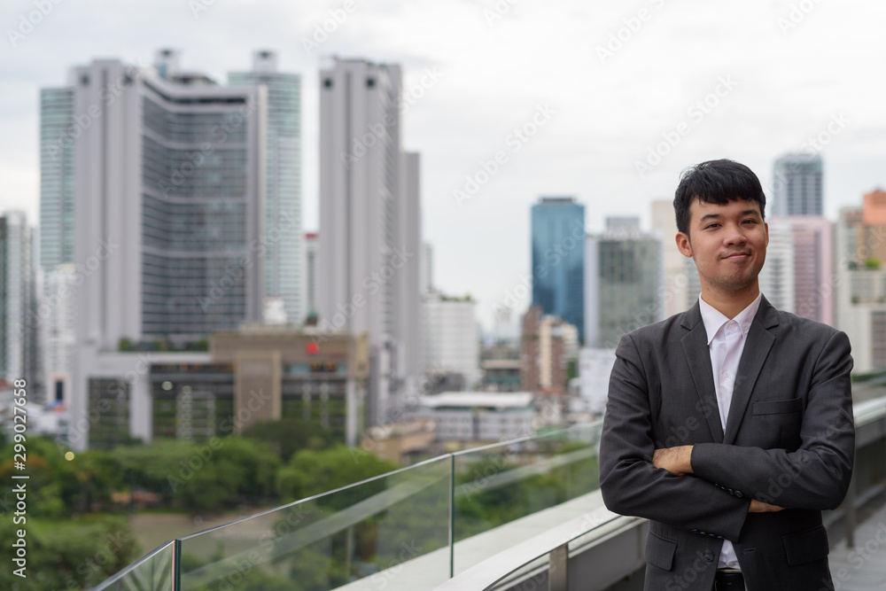 Portrait of young Asian businessman against view of the city Portrait of young Asian businessman against view of the city
