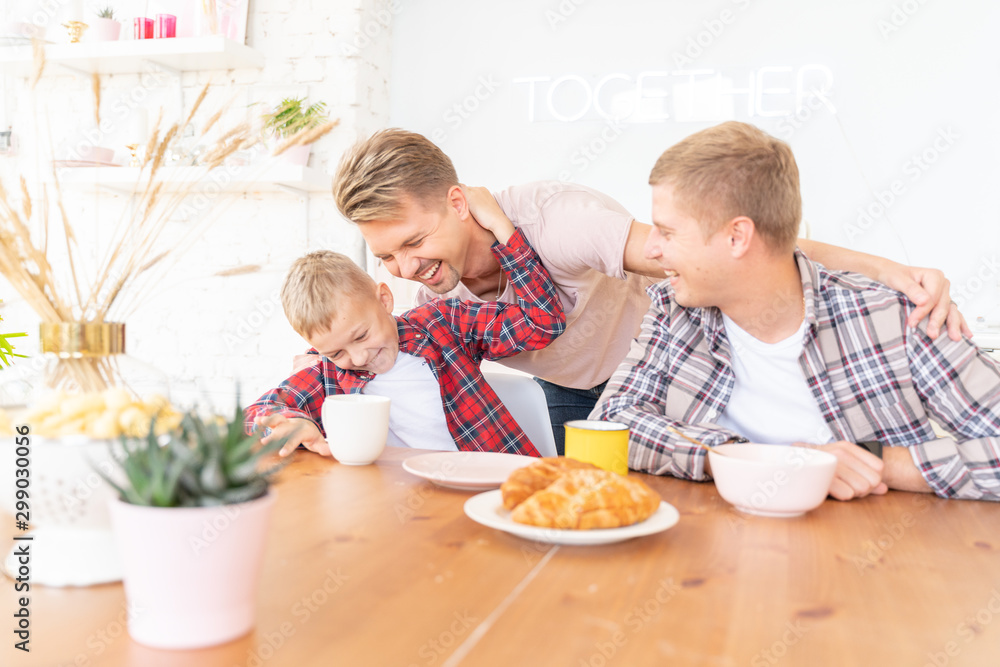 Happy young fathers and son have breakfast in the kitchen, gay family with a child, time together, parenting in homosexual families concept Happy young fathers and son have breakfast in the kitchen, gay family with a child, time together, parenting in homosexual families concept